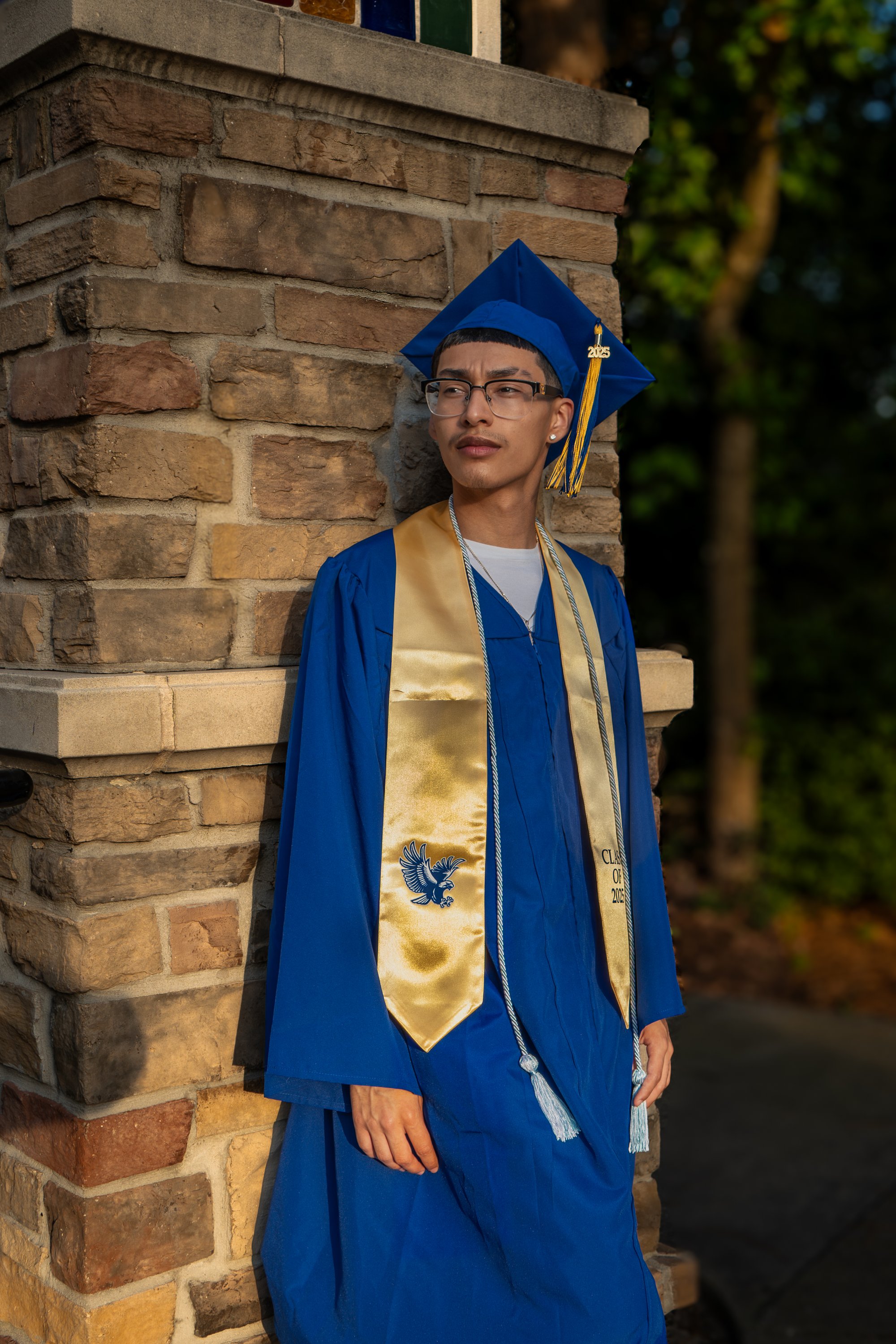 Graduate standing by brick pillar, blue gown