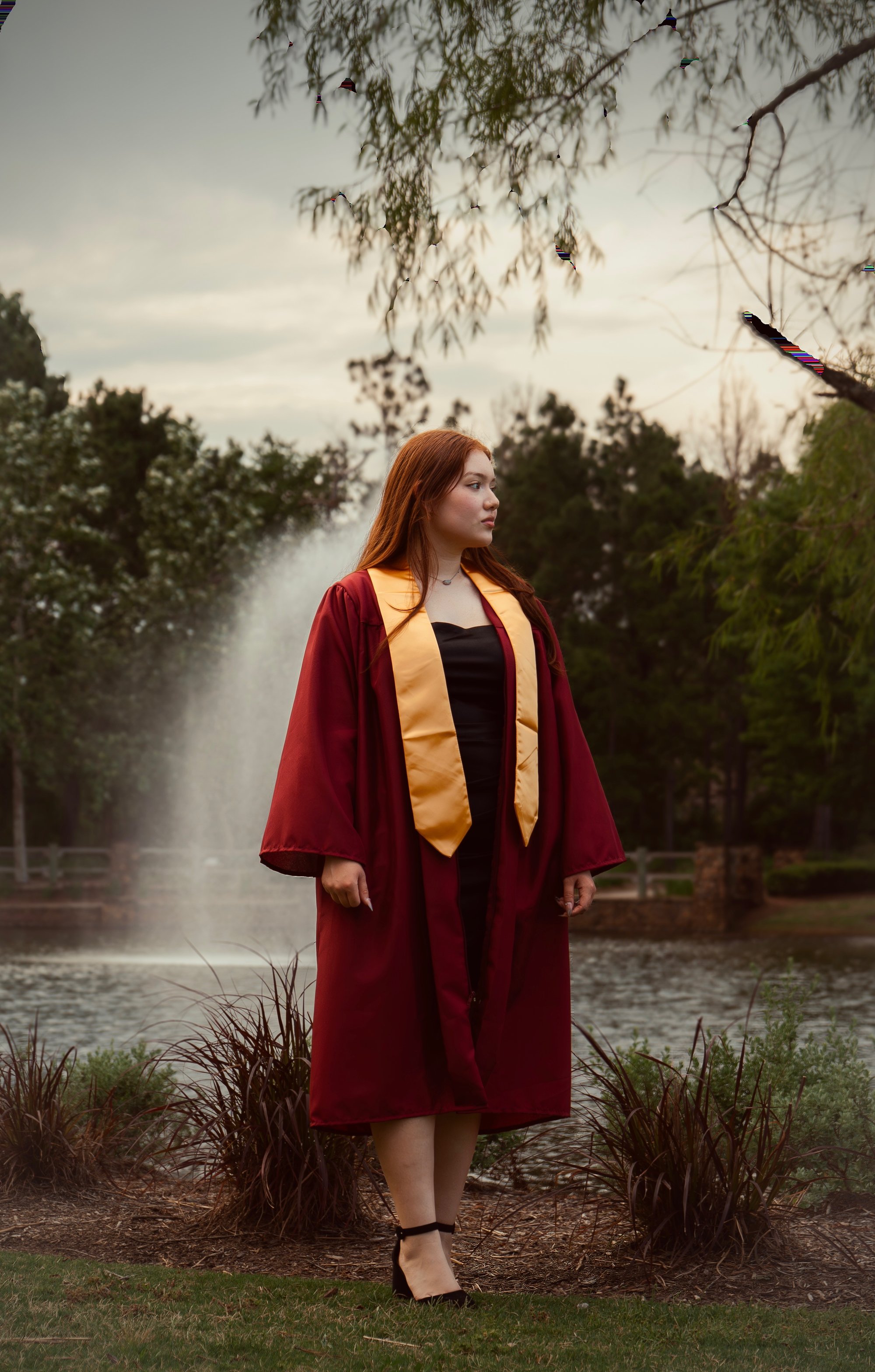 Graduate walking path by fountain, maroon gown