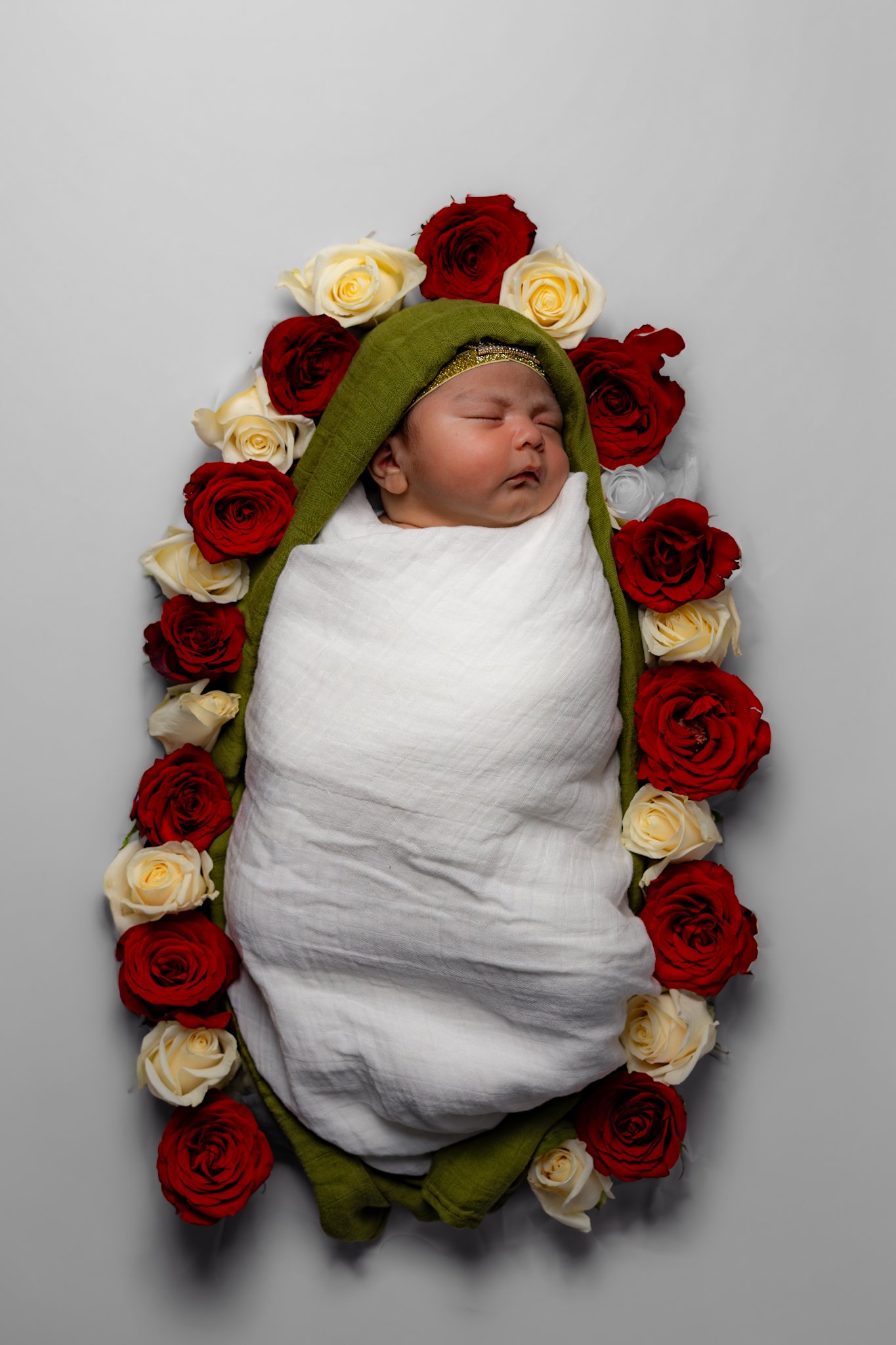 Sleeping newborn swaddled in white, framed by a rose wreath